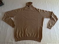 Flat laid camel cashmere turtleneck sweater showing full front view highlighting color, shape, and ribbing details.