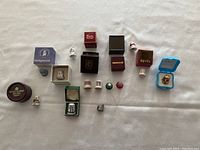 Thimbles arranged on white cloth background showing various branded boxes including Royal Albert, Wedgwood, Spode, and others with thimbles in front or beside the boxes.