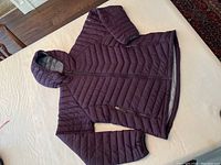 Full view of the deep purple Columbia winter jacket with hood lying flat on a white surface showing outer quilted front.