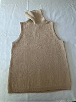Full view of sleeveless turtleneck sweater laid flat on surface showing light camel knit fabric.