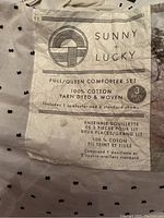 Close-up photo of the Sunny + Lucky Full/Queen comforter set packaging showing brand, composition (100% cotton), and piece count (3 pieces)