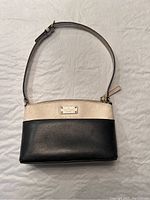 Full front view of the Kate Spade cream and navy leather purse with shoulder strap laid flat on neutral background.