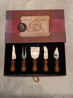 Photo of the La Vie Splendide Rustica cheese cutter set in original box showing all five tools with wooden handles and stainless steel blades.