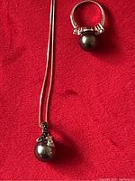 Photo showing the pearl necklace and ring on red fabric background, highlighting the black pearl-like stones and CZ accents on both items
