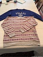 Photo of both sweaters laid flat on table: women's grey Fair Isle sweater on top of men's cobalt blue Polo RL Academy sweatshirt.