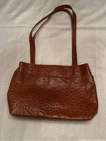 Exterior view of a camel colored ostrich leather purse with textured pattern and long shoulder strap.