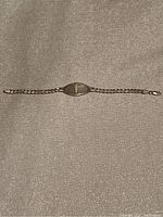 Full view of the silver Medic Alert bracelet laid flat on a light textured fabric surface showing the chain and central oval plate.