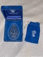 Full view of the crystal ornament inside the open blue velvet presentation box alongside the velvet pouch.