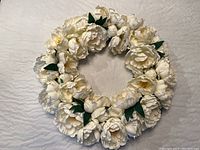 Top-down view of full white floral wreath with green leaves, showing detail and overall condition.