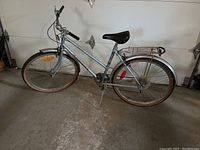 Full side view of Supercycle Commuter Six woman's bicycle showing silver frame, black rear rack, black kickstand, and brown sidewall tires.
