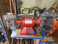 Full view of the red Baldor grinder buffer with grinding and buffing wheels on a wooden table surrounded by tools and equipment