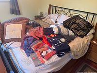 Photo of bed piled with all items including pillows, blankets, throws, Sunbeam heated mattress pad and sheets.