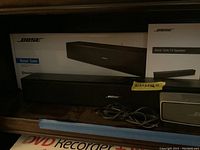 Bose Solo TV Speaker with its original box, black rectangular soundbar with Bose logo on front, cables beside the speaker.
