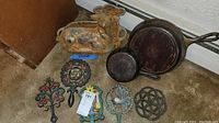 Overview showing two cast iron skillets, lamb-shaped mold, and five decorative trivets on floor.