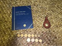 Blue Indian Head Cent coin collection book with 18 coins, two foreign coin bracelets displayed next to a worn leather key fob with an embedded, damaged Buffalo nickel coin visible.