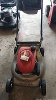 Front view of the Honda lawn mower showing the handle, wheels, and red engine cover.