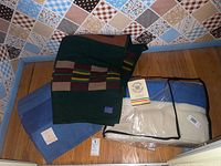 Three folded blankets: green patterned Beaver State Pendleton, solid blue Hudson’s Bay with tag, cream Hudson’s Bay with blue stripes in plastic