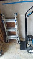 Werner aluminum foldable ladder leaning against wall next to Craftsman hand truck, both on a garage floor.