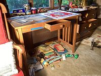 Full view of mission style oak table or desk with drawer, showing worn surface and drawer open. Various papers and miscellaneous items on and beneath table not included.
