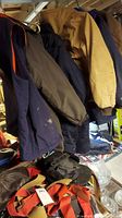 Photo of multiple winter jackets including navy, brown, and caramel color jackets hung on a rack showing visible wear and damage