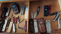 Full drawer view showing multiple multi tools, pocket knives, cases, and small cutters organized in a wood divider.