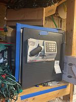 Closed Sentry Safe on wooden shelf surrounded by other items, showing front with handle and keypad lock.