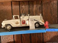 Side view of white metal Tonka toy fire truck with hose and red fire hydrant on wooden shelf with size note.
