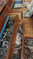 Open wooden drawers showing a collection of vintage black and white photographs, yearbooks, and loose photos piled inside.