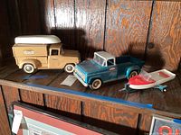 All lot items on shelf: tan camper truck with canoe, teal open truck, boat on trailer
