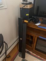 Two Vizio sound bars leaning against a wooden cabinet, along with a subwoofer and wires.