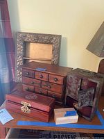 Arrangement of three wooden boxes on surface including carved drawer box, rectangular box with clasp, and damaged shadow box