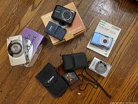 All four Canon point-and-shoot cameras with original boxes and three camera pouches on floor