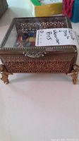Rectangular cherub jewelry dish with ornate metal sides and legs, glass lid missing, with handwritten note