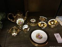 Full set arranged on wooden surface showing all components: teapot, creamer, sugar bowl, plates, and cups with saucers.