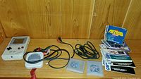 Photo shows original Nintendo Game Boy console, cables, game cartridges including Tetris, and instruction manuals on wooden surface.