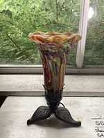 Front view of colorful hand blown glass lamp shade with flared ruffled top on metal leaf-shaped base.