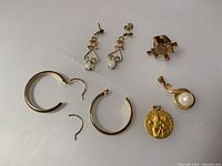 Full overview of two pairs of gold earrings including opal drop earrings, gold hoop earrings, single hoop earring, and two gold pendants.