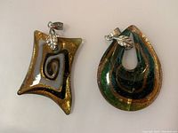 Two Murano glass pendants laid side by side showing overall shapes, colors, clasp details
