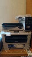 Brother MFC-7360N printer with unopened toner cartridge and operating manual on top.