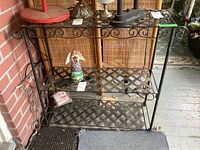 Metal shelf against a brick wall showing two lattice shelves and decorative scrollwork on top and sides.