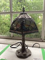 Full view of stained glass lamp showing metal base and floral patterned stained glass shade with pink and purple glass panels.