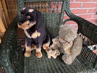 Photo showing a stuffed black and tan dog and a brown bear with two small cubs on a green wicker chair.