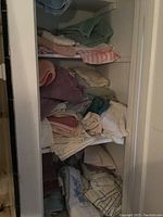 Shelf with piles of folded bath towels, facecloths, and table linens in various colors and patterns, showing wear.