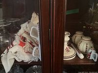 Shelf with embroidered cloths, ceramic mugs, candlesticks, spice jars with lids, and dried wheat stalks all featuring Ukrainian folk motifs.