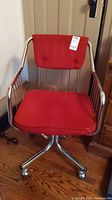 Front view of vintage office chair showing red tufted fabric seat and backrest on chrome metal frame with caster wheels.