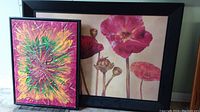 Two framed artworks leaning against a wall on the floor, poppy painting and starburst painting
