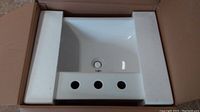 Photo of white ceramic rectangular drop-in sink placed inside protective foam in original box.