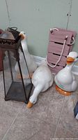 Photo showing three white ceramic ducks and one metal lantern, display of the figurines and lantern size and shape.