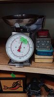 Photo of kitchen scale with metal bowl and four advertising tins stacked to the right, showing the size and condition of items with visible scratches.
