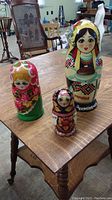 Photo showing all three sets of nesting dolls on a wooden table, arranged upright including the largest doll from the Ukrainian themed set with colorful patterns and text.
